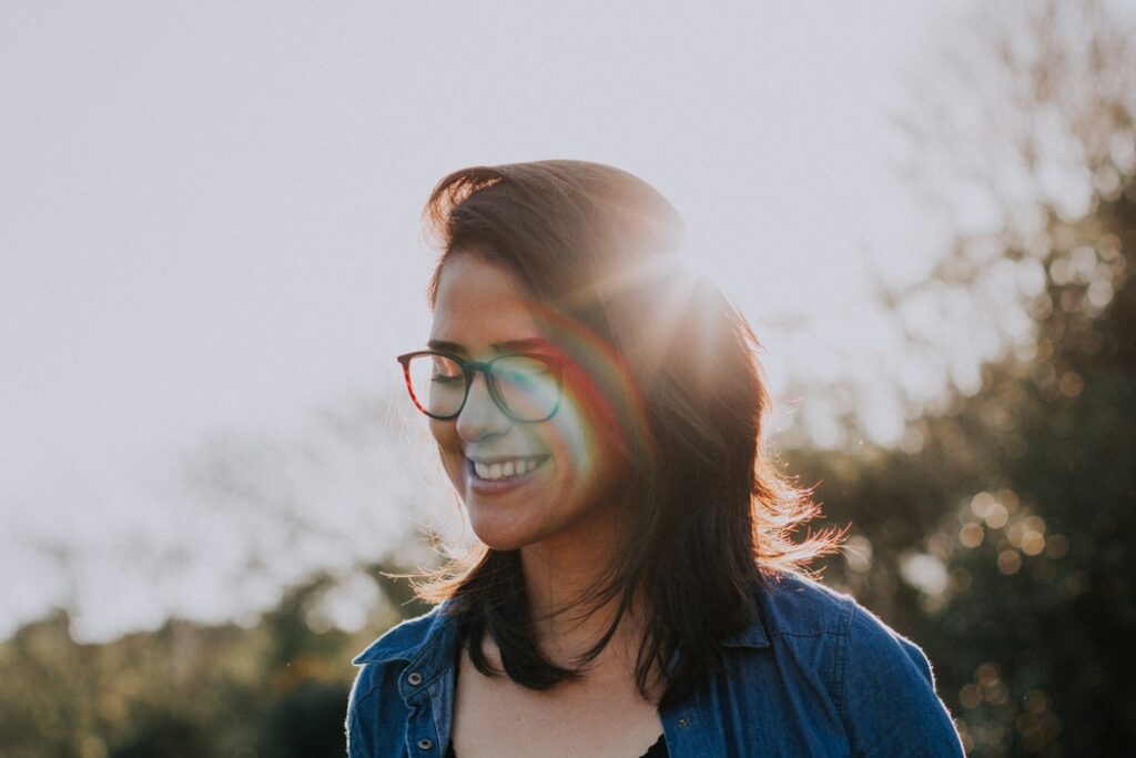 Smiling woman with glasses outdoors in warm sunlight, looking hopeful and at peace during recovery.