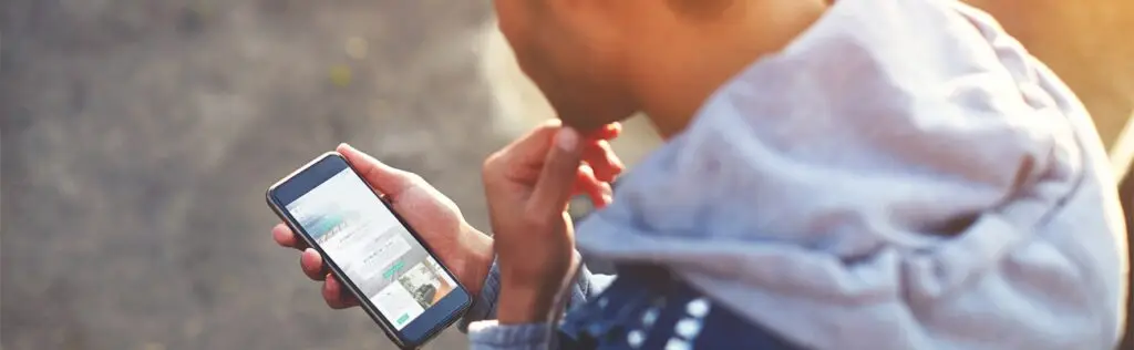 Person sitting outdoors looking at a smartphone, researching addiction treatment options.