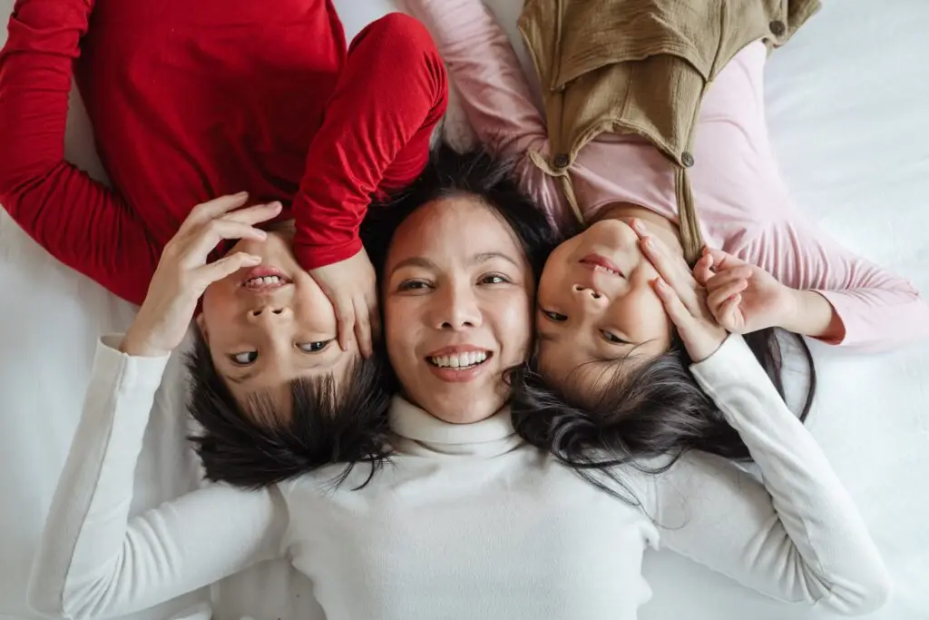 Smiling mother lying with her two children, reconnecting joyfully after recovery and family healing.